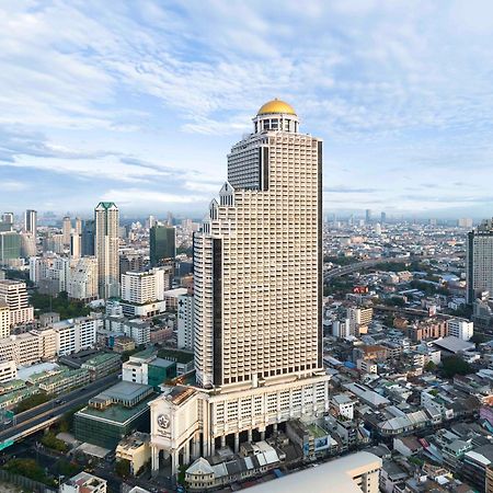 Hotel Lebua At State Tower Bangkok Esterno foto The photo shows a tall, modern skyscraper with a distinctive golden dome on the top. It is situated amidst a bustling urban cityscape, featuring various other buildings of different heights and designs. The surrounding area appears densely populated,