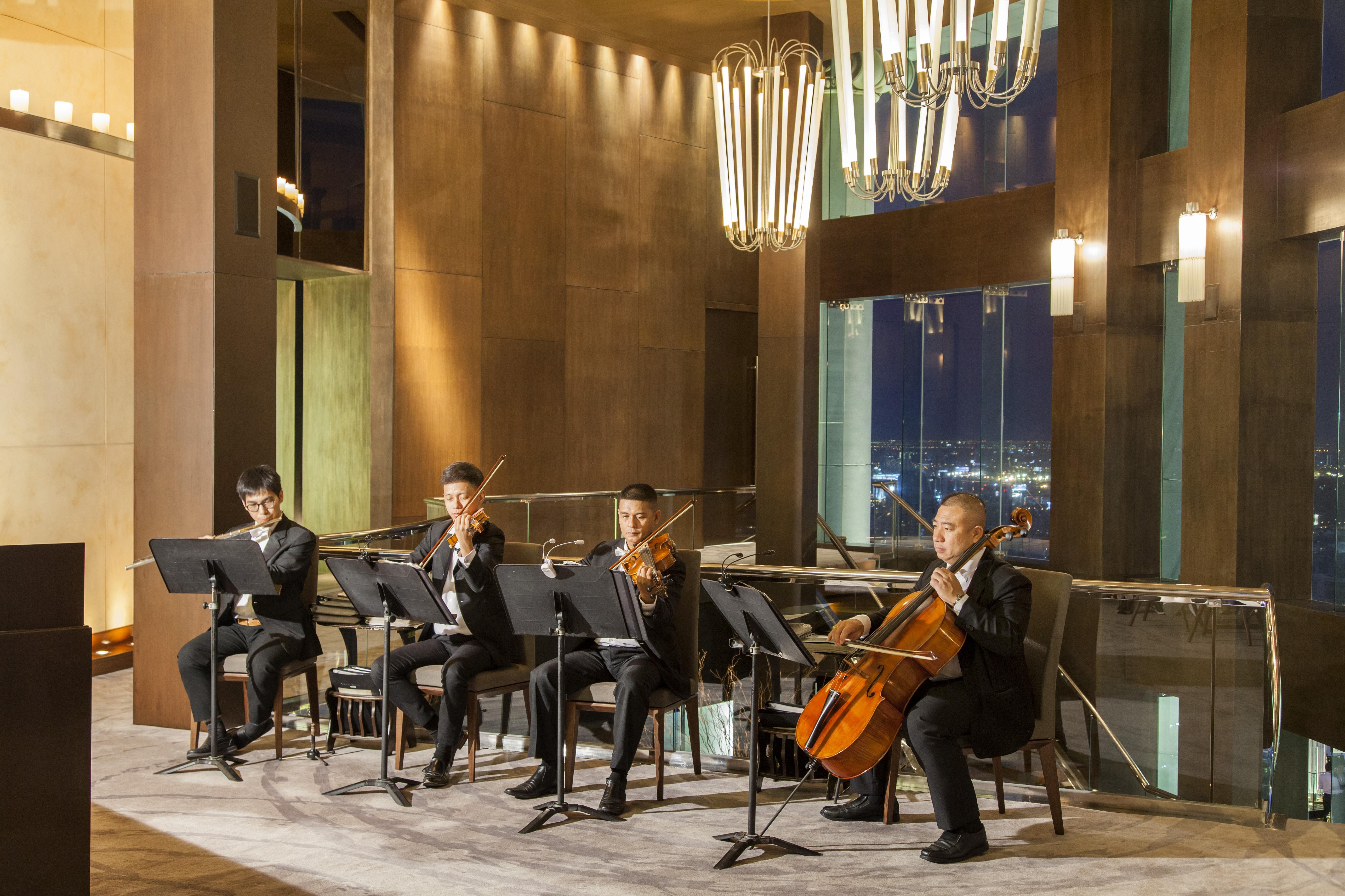 Hotel Lebua At State Tower Bangkok Esterno foto The photo shows a string quartet performance taking place in a sophisticated indoor setting. Four musicians are seated, each playing a different string instrument: two are playing violins, one is playing a viola, and one is playing a cello. They are 